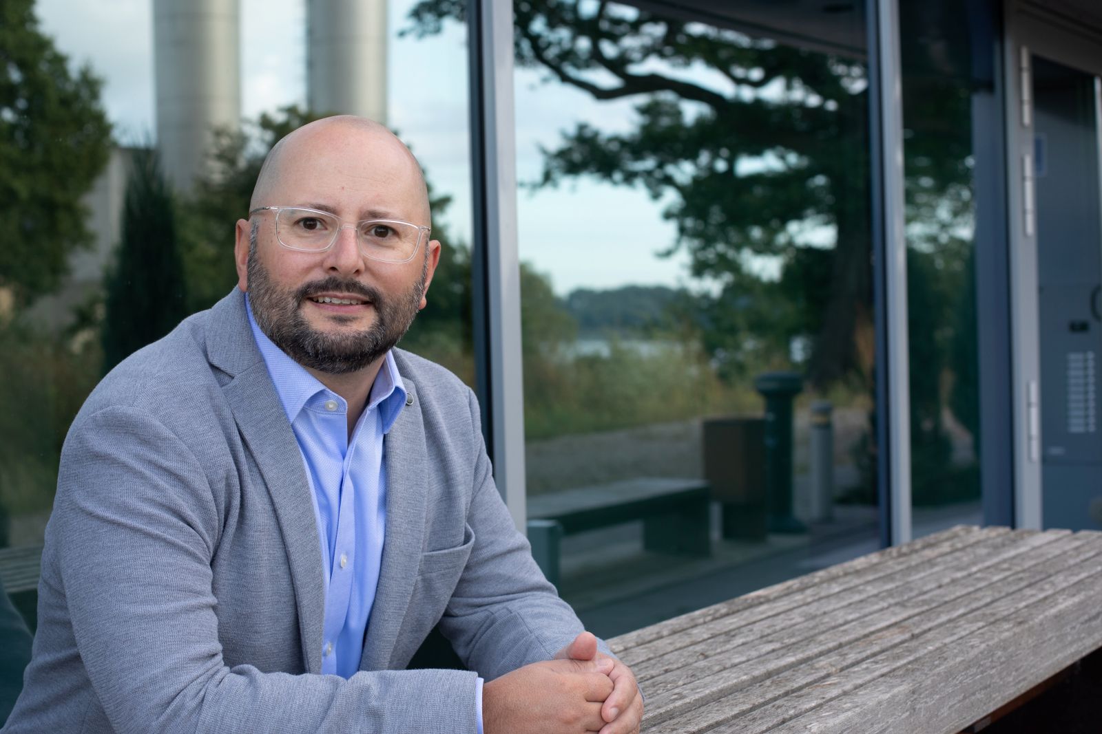 Dr. Jens Träger, Gründer von Truinorva, im grauen Sakko vor Glasfassade; Porträt am Holztisch im Freien.