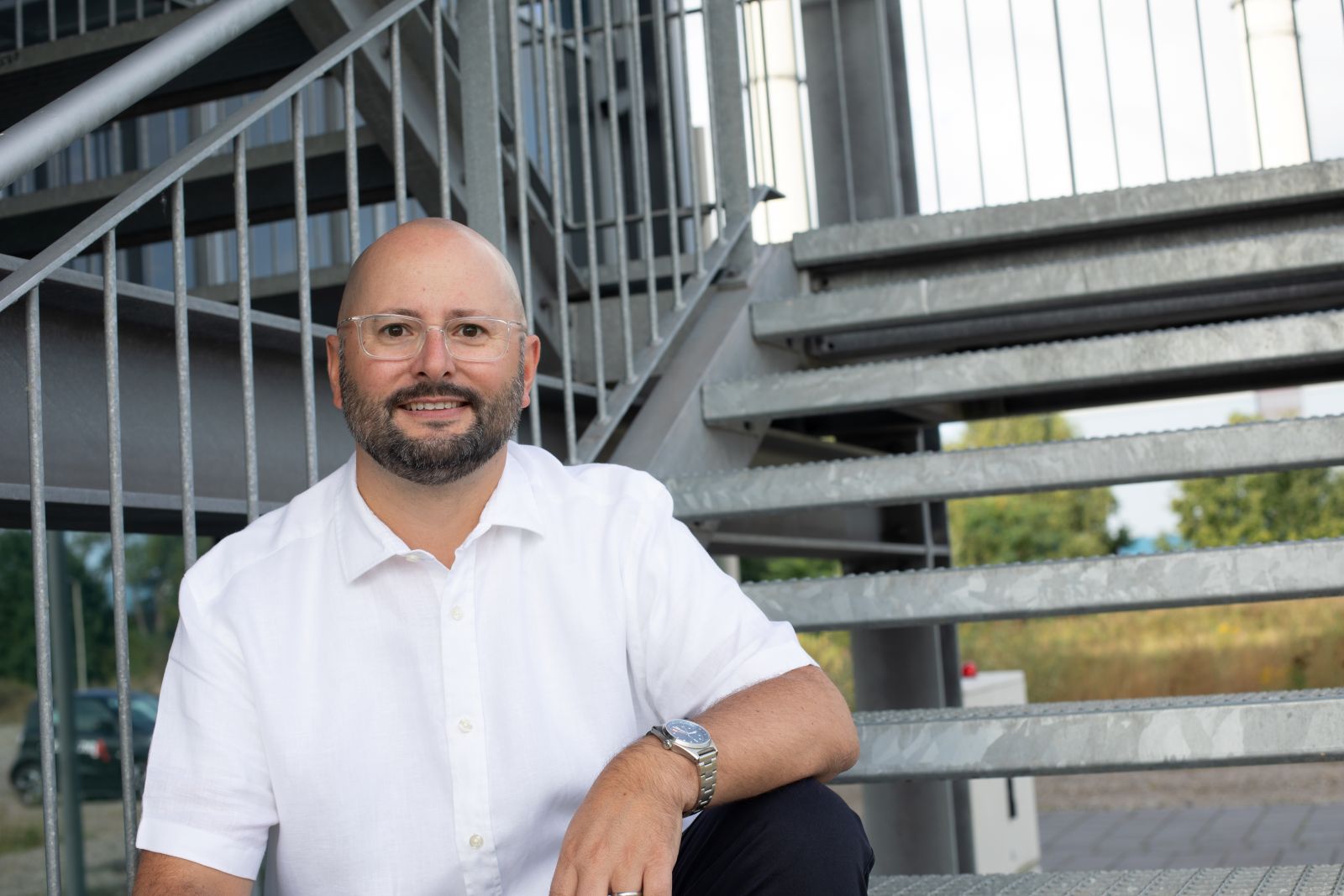 Dr. Jens Träger, Gründer von Truinorva, im weißen Hemd auf einer Metalltreppe; freundliches Porträt im Industrieumfeld.